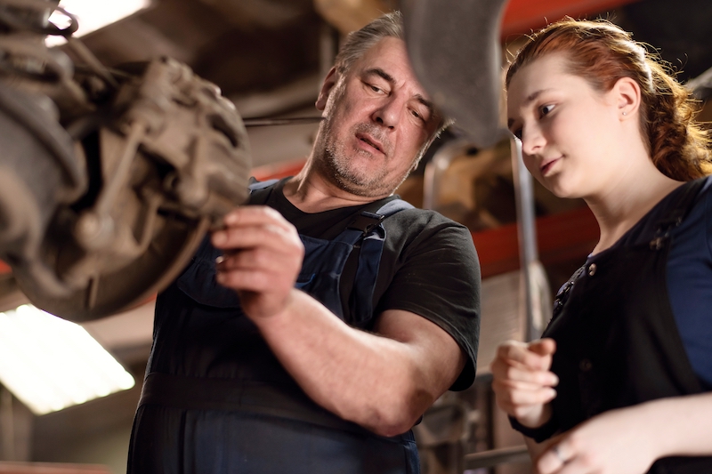 Staff Training Techniques, older male mechanic training young female mechanic in a garage.